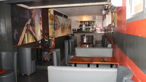 Un restaurante con asientos tipo banca acolchados en gris, mesas de madera y un área de bar con estantes llenos de botellas.