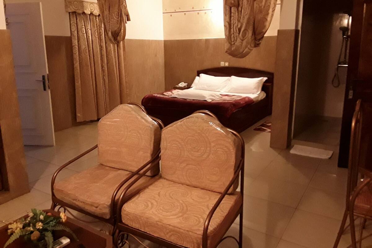 A hotel room with a bed, a chair, a bedside table, and curtains.