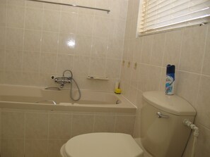Un baño con bañera, inodoro y ventana con persianas.