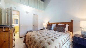 Quarto com cama, mesas de cabeceira, cômoda e espelho.