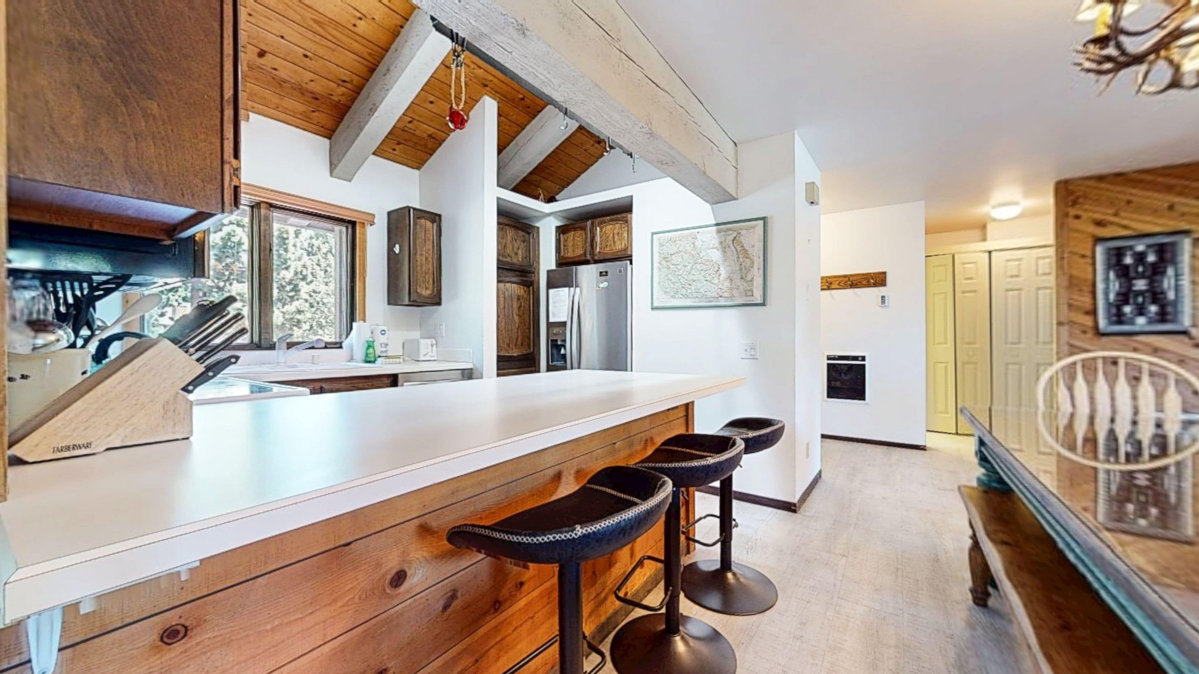 A kitchen with wooden cabinets, a large island with stools, and a hanging light fixture.