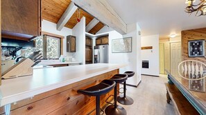 Une cuisine avec des meubles de rangement en bois, un grand îlot central doté de tabourets et un luminaire suspendu.