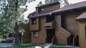 A modern multi-story building with a wooden facade, a covered outdoor area, and a staircase leading to the entrance.