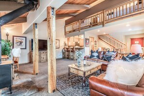 A spacious living area with a high ceiling, wooden beams, a staircase, and a cozy seating arrangement. - Courchevel 14 Remodeled Light and Bright Mountain Cabin, Walk to Canyon Lodge Slopes by RedAwning (Mammoth Lakes)