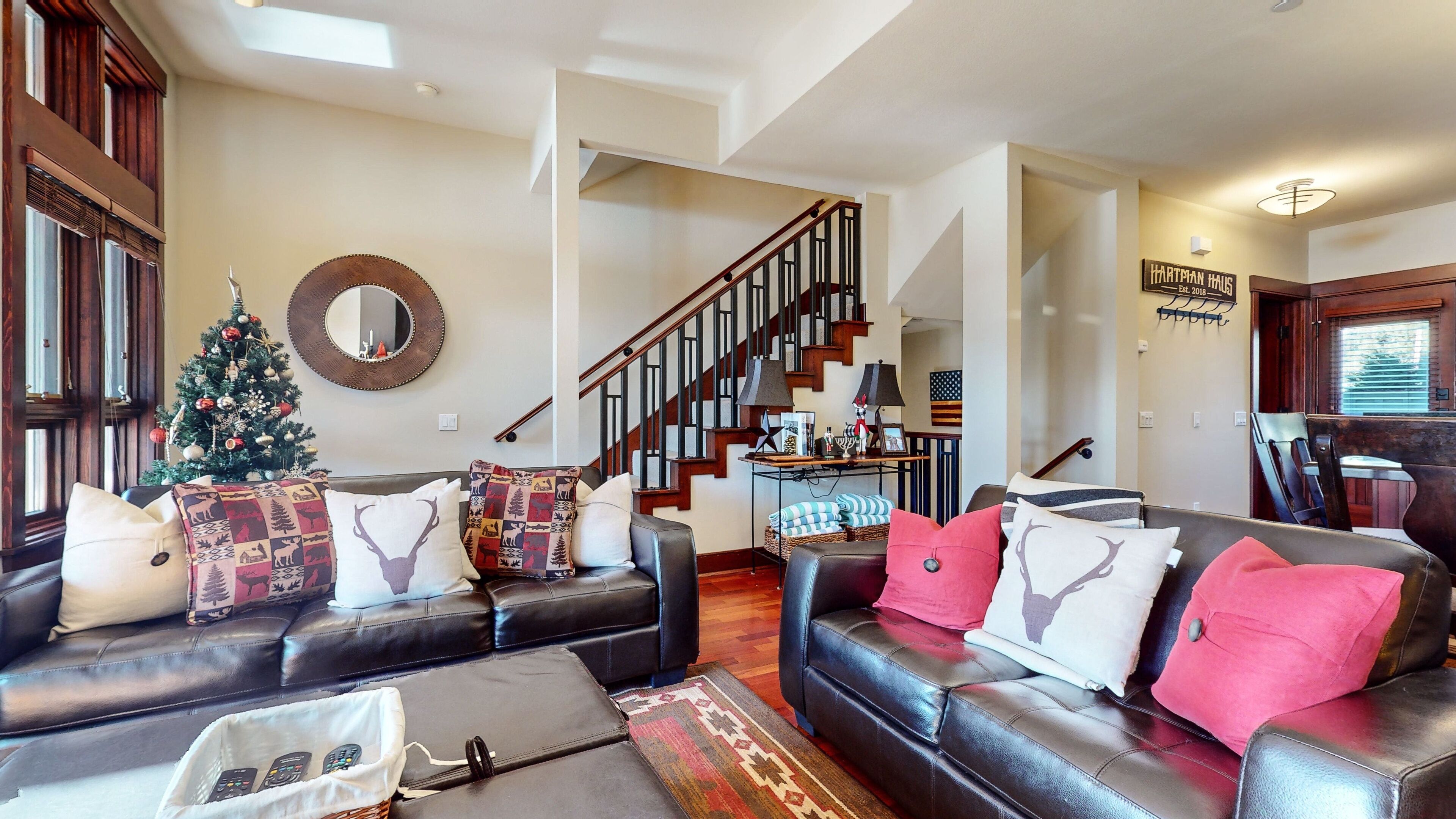 A spacious living room with leather sofas, a Christmas tree, and a staircase leading to another level.