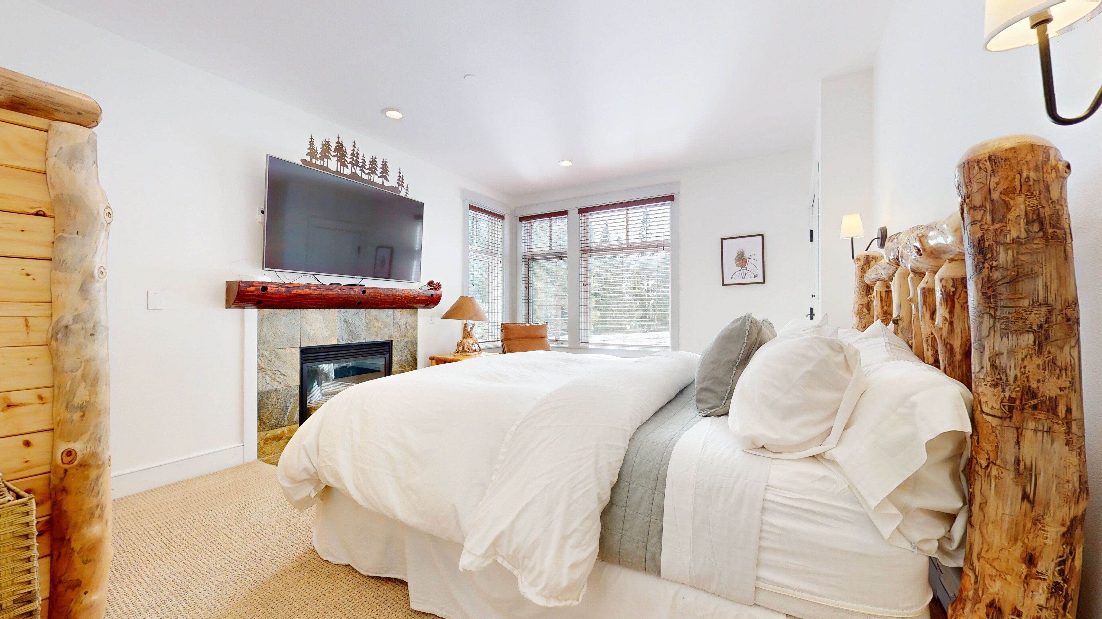 A bedroom with a large bed, a fireplace, and a TV mounted on the wall.