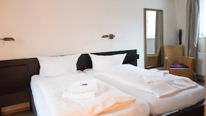 Habitación de hotel con dos camas, un espejo grande, una silla y una lámpara fijada a la pared.