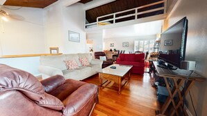 A spacious living area with a high ceiling, a large TV, and a cozy seating arrangement including a sofa and a leather armchair. - Sierra Manors 8 Pet-Friendly, Short Walk to the Shuttle, Spacious, Centrally Located by RedAwning (Mammoth Lakes)
