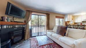 Una sala de estar con chimenea, un sofá, un televisor y vistas al exterior.