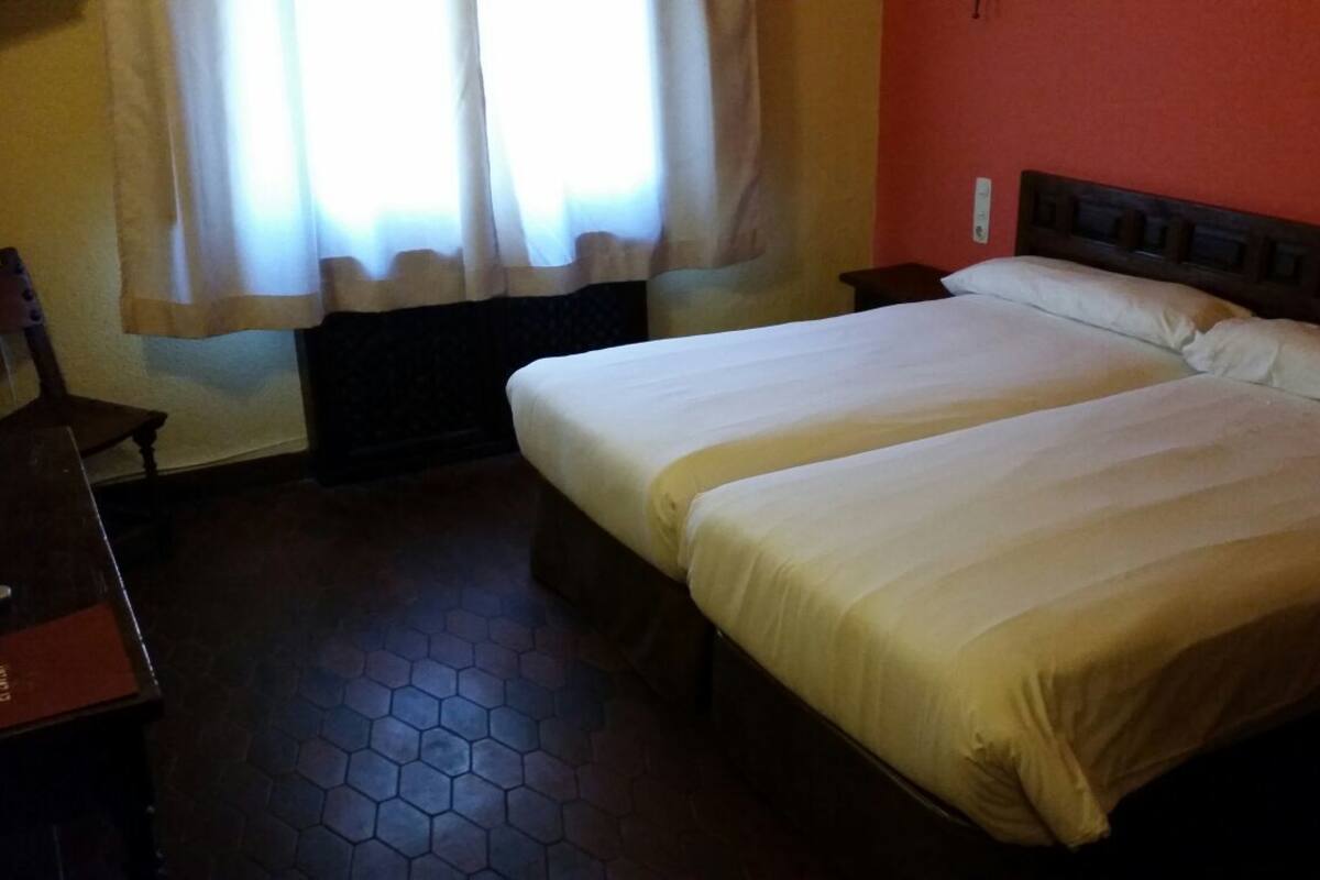 Ein Hotelzimmer mit zwei Betten, einem Holzkopfende, einem Holzstuhl und einem Fliesenboden.