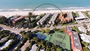 An aerial view of a coastal hotel with multiple buildings, a tennis court, and a beach in the background. - Waters Edge 110n 2 Bedroom Condo by RedAwning (Holmes Beach)