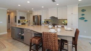 A spacious kitchen with a large island, white cabinetry, and a tiled backsplash. - Waters Edge 110n 2 Bedroom Condo by RedAwning (Holmes Beach)