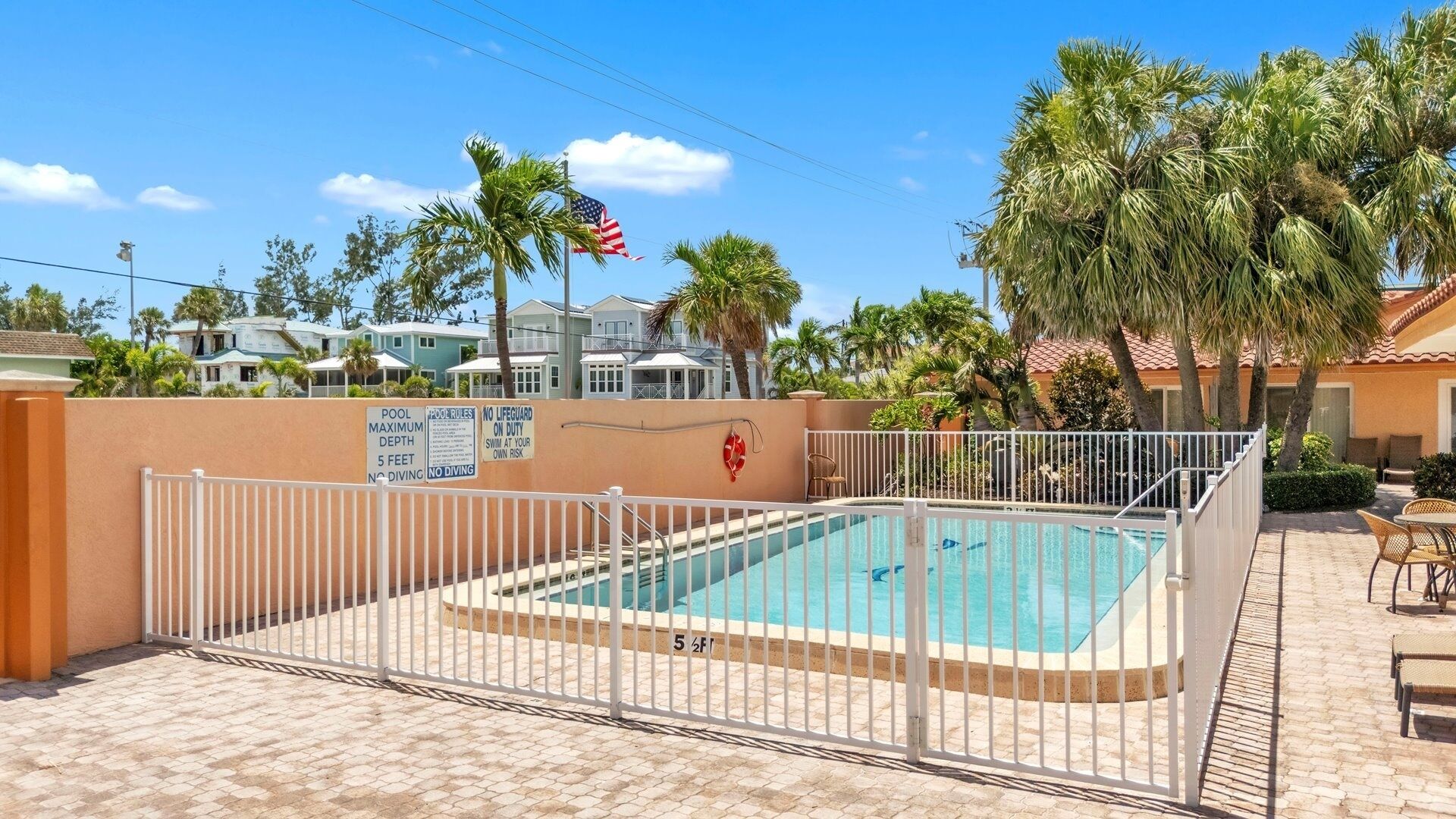 A swimming pool with a white fence, palm trees, and a lifeguard flag.