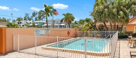 A swimming pool with a white fence, palm trees, and a lifeguard flag.