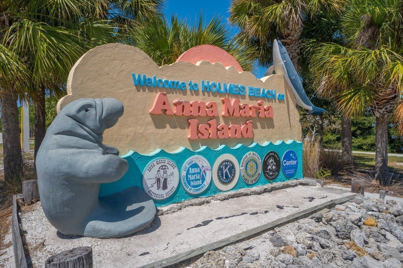 A welcome sign for Holmes Beach, Anna Maria Island, featuring a seal sculpture and various historical and community logos.