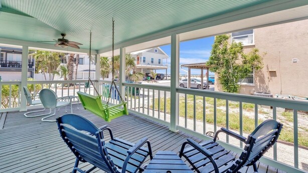 A covered outdoor area with a swing chair, a bench, and a view of a residential street. - Marmalade Mermaid 3 Bedroom Home by RedAwning (Bradenton Beach)