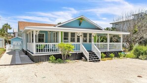 A coastal house with a covered porch, a small front yard, and a sandy driveway. - Marmalade Mermaid 3 Bedroom Home by RedAwning (Bradenton Beach)