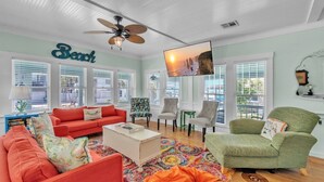 A living room with a red sofa, green armchair, and a ceiling fan. - Marmalade Mermaid 3 Bedroom Home by RedAwning (Bradenton Beach)