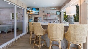 A bar area with wicker chairs, a television displaying a beach scene, and a sign reading "FREE DRINKS."