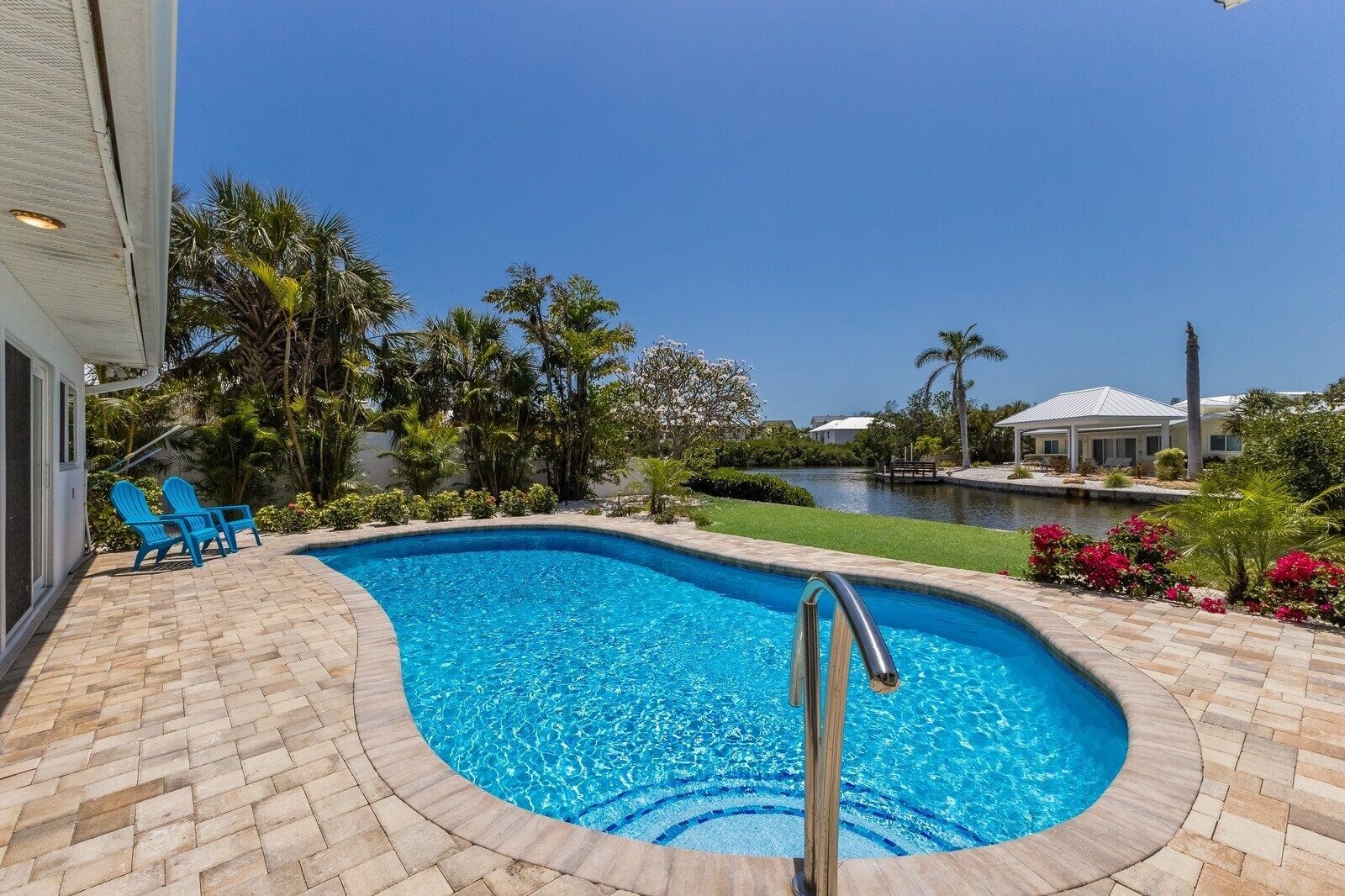 A swimming pool with a clear blue water feature, surrounded by a brick patio and lush greenery.