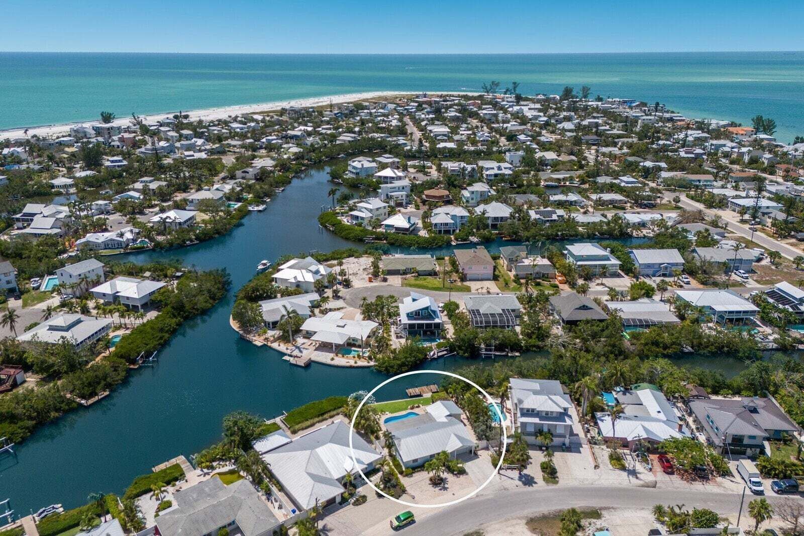 An aerial view of a coastal residential area with houses, a marina, and a beach.