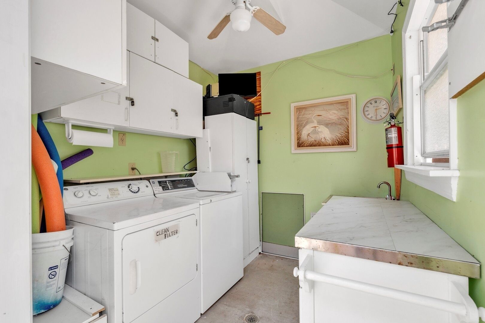 A compact laundry room with a washing machine, dryer, and stacked surfboards.