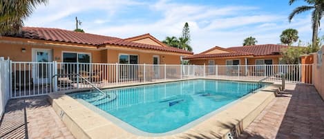 Una piscina con cerca blanca, rodeada de edificios con tejados rojos.