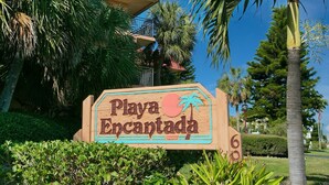 A wooden sign with the text "Playa Encantada" and a palm tree graphic. - Playa Encantada 214 2 Bedroom Condo by RedAwning (Holmes Beach)