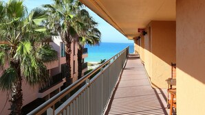 A balcony with a view of the sea, palm trees, and a building with a sign that reads "The Exterminator". - Playa Encantada 214 2 Bedroom Condo by RedAwning (Holmes Beach)