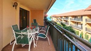 A balcony with a table and chairs, a view of a building with balconies, and a clear sky. - Playa Encantada 214 2 Bedroom Condo by RedAwning (Holmes Beach)