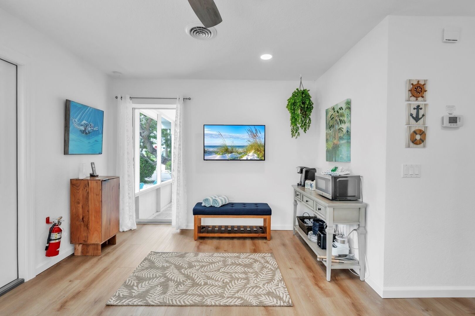 A modern living room with a wooden bench, a television, and a small kitchenette.