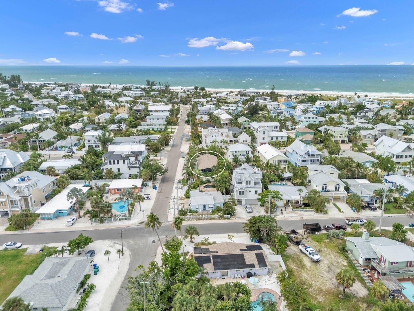 A coastal residential area with houses, a road, and a beach in the background.