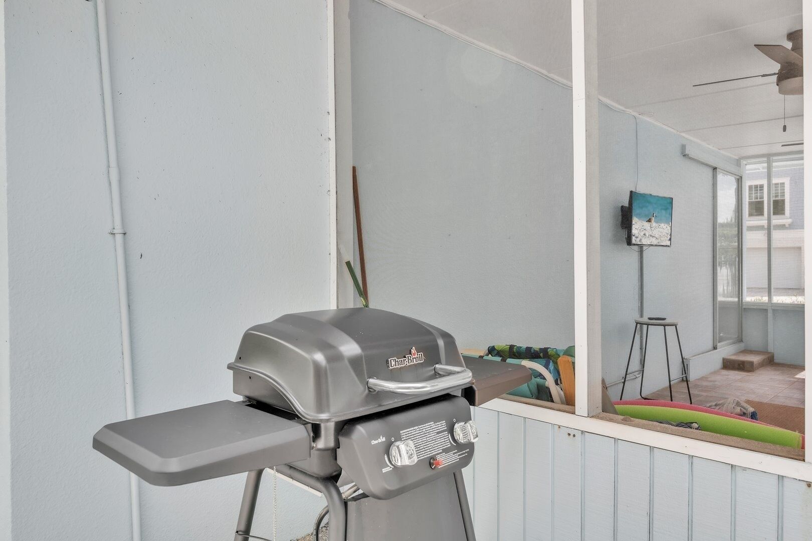 A balcony with a barbecue grill, a small stool, and a painting on the wall.