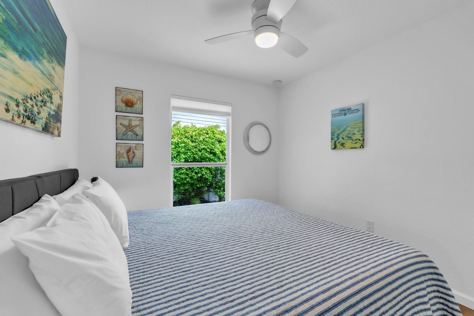 Quarto com cama, ventilador de teto, janela com persianas e quadros nas paredes.