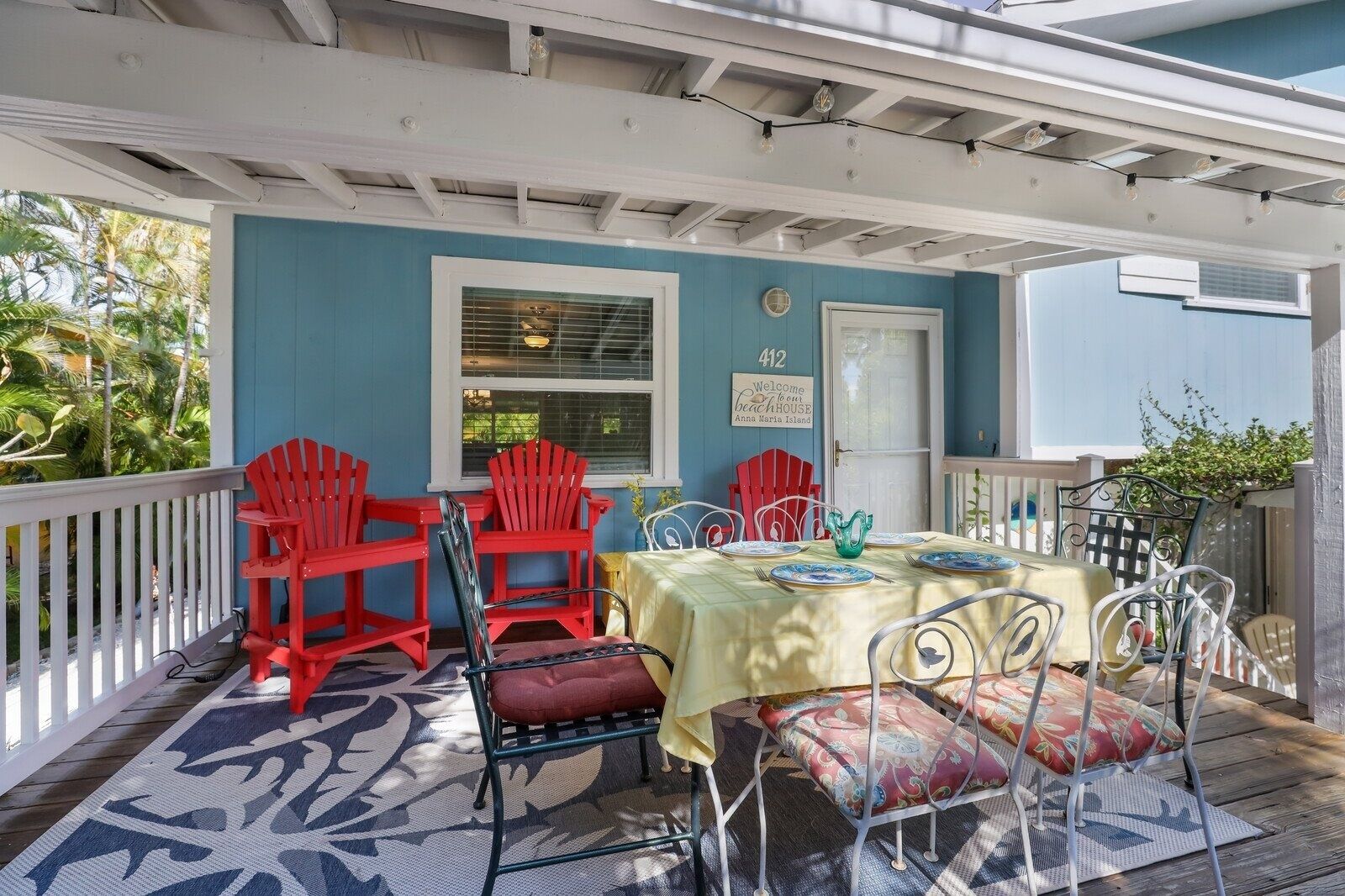 A covered outdoor dining area with a table set for four, surrounded by red chairs and a red bench.