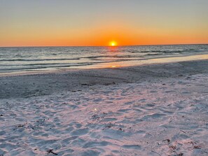 A beach at sunset with the sun setting over the ocean. - Beach Breeze Hideaway 2 Bedroom Villa by RedAwning (Holmes Beach)