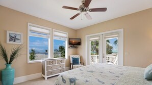 A bedroom with a bed, a ceiling fan, a dresser, a chair, a TV, and large windows with a view of the outdoors. - Blue Water Escape 3 Bedroom Villa by RedAwning (Bradenton Beach)