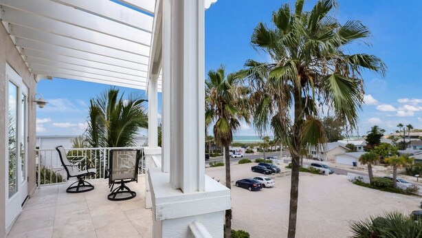 A balcony with two chairs and a view of a beach and parked cars. - Blue Water Escape 3 Bedroom Villa by RedAwning (Bradenton Beach)