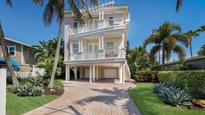 A two-story house with a covered front porch, a garage, and a well-maintained lawn with palm trees. - Blue Water Escape 3 Bedroom Villa by RedAwning (Bradenton Beach)