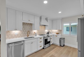 A modern kitchen with white cabinetry, stainless steel appliances, and a wooden floor.