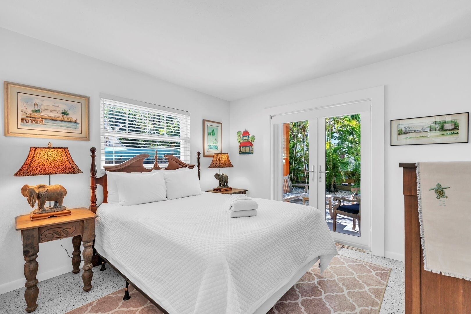 A bedroom with a large bed, two bedside tables with lamps, a wooden headboard, and a view of a garden through a sliding glass door.