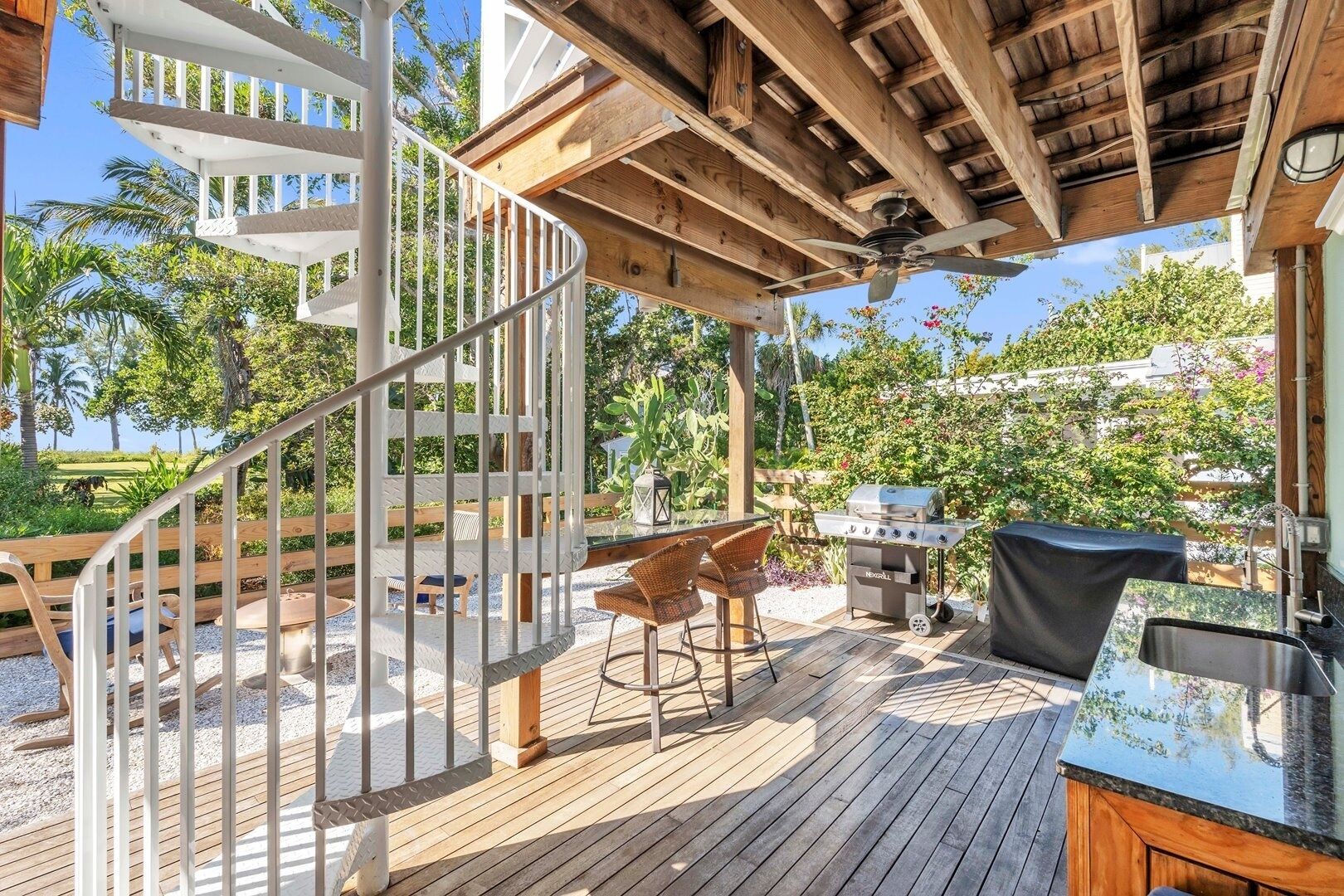 Eine Holzterrasse mit Wendeltreppe, Sitzgelegenheiten im Freien, einem Grill und Blick auf einen Golfplatz.