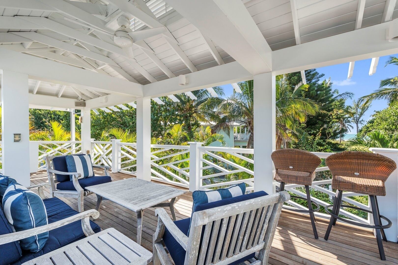 A covered outdoor seating area with wooden furniture and white railings, overlooking a tropical landscape.