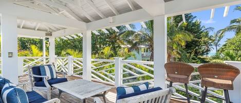 A covered outdoor seating area with wooden furniture and white railings, overlooking a tropical landscape.