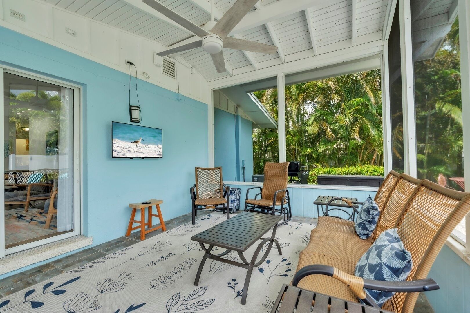 A covered outdoor seating area with wicker furniture, a small table, and a television mounted on the wall.