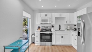 A modern kitchen with white cabinets, stainless steel appliances, and a blue bench by the window. - Minnow 2 2 Bedroom Villa by RedAwning (Anna Maria)