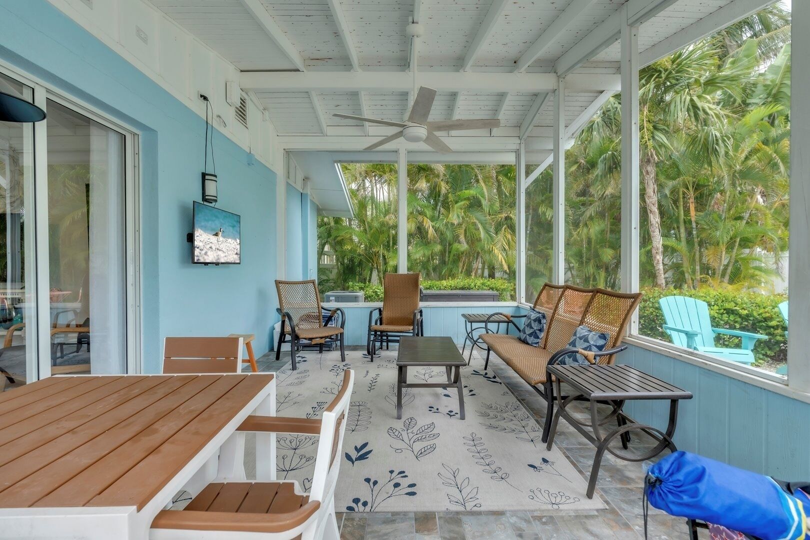 A covered outdoor seating area with wooden furniture, a ceiling fan, and a view of lush greenery.