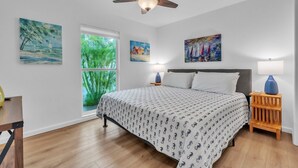 A bedroom with a bed, a ceiling fan, a window with a view of greenery, and artwork on the walls. - Minnow 2 2 Bedroom Villa by RedAwning (Anna Maria)