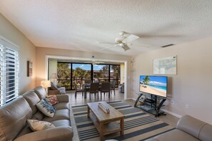 Una sala de estar con sofá, mesa de centro, televisor y un balcón con mobiliario exterior.