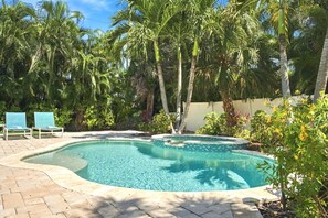 Una piscina de borde curvo, rodeada de palmeras y un patio de ladrillo.